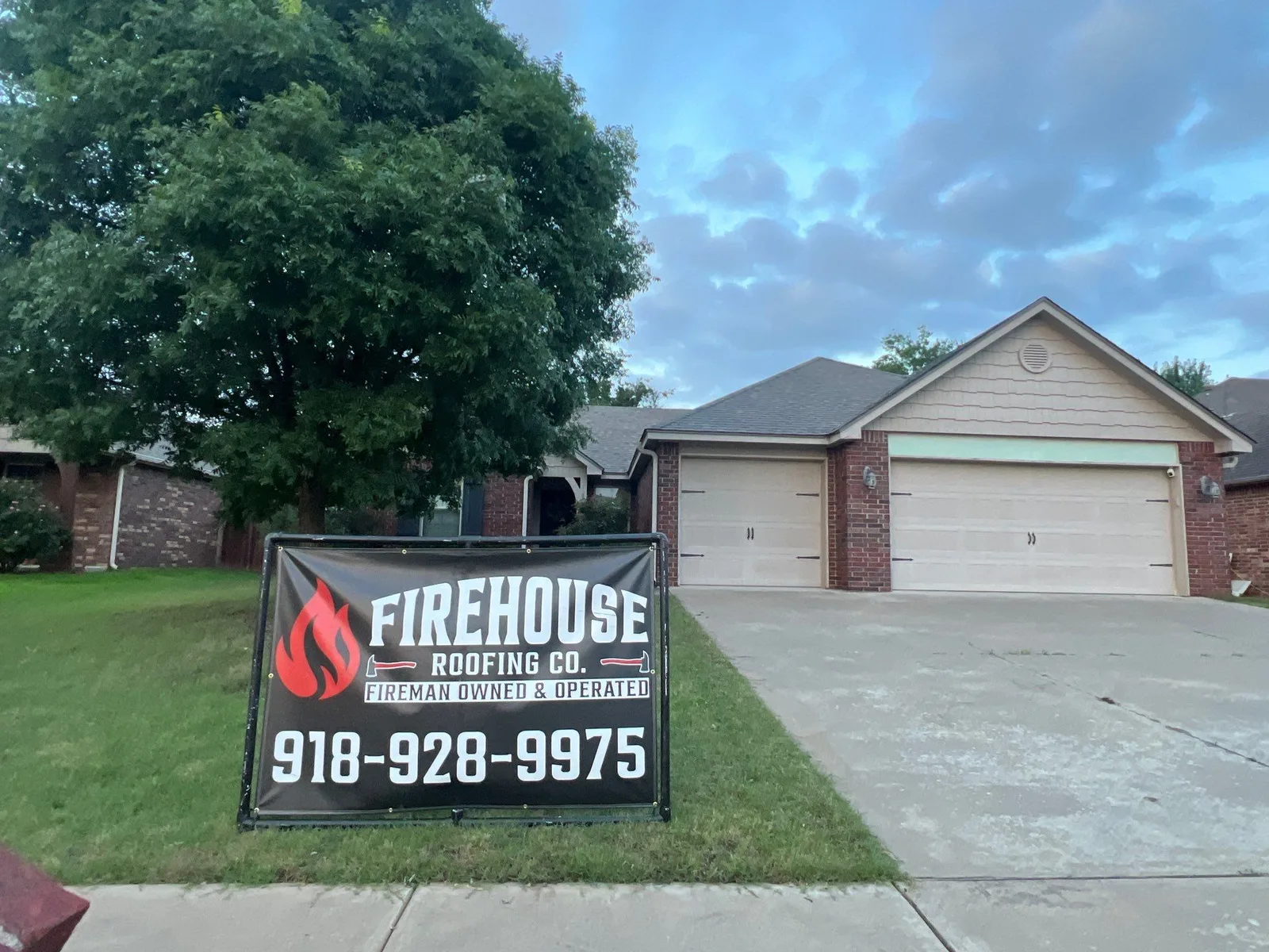 Collinsville brick ranch home at dusk with FireHouse Roofing yard banner after a completed roof project
