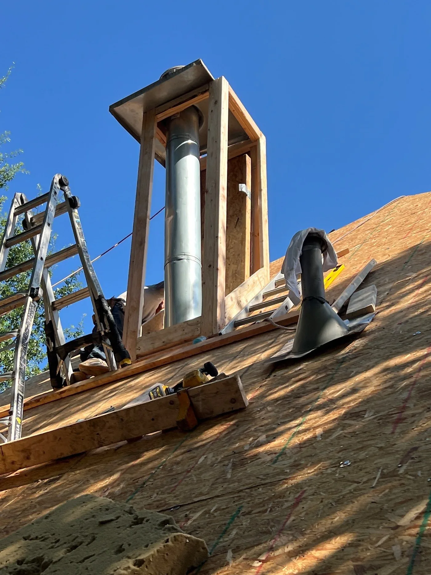 Chimney framing and flashing prep on a Tulsa roof replacement, decking exposed and pipe boot in place