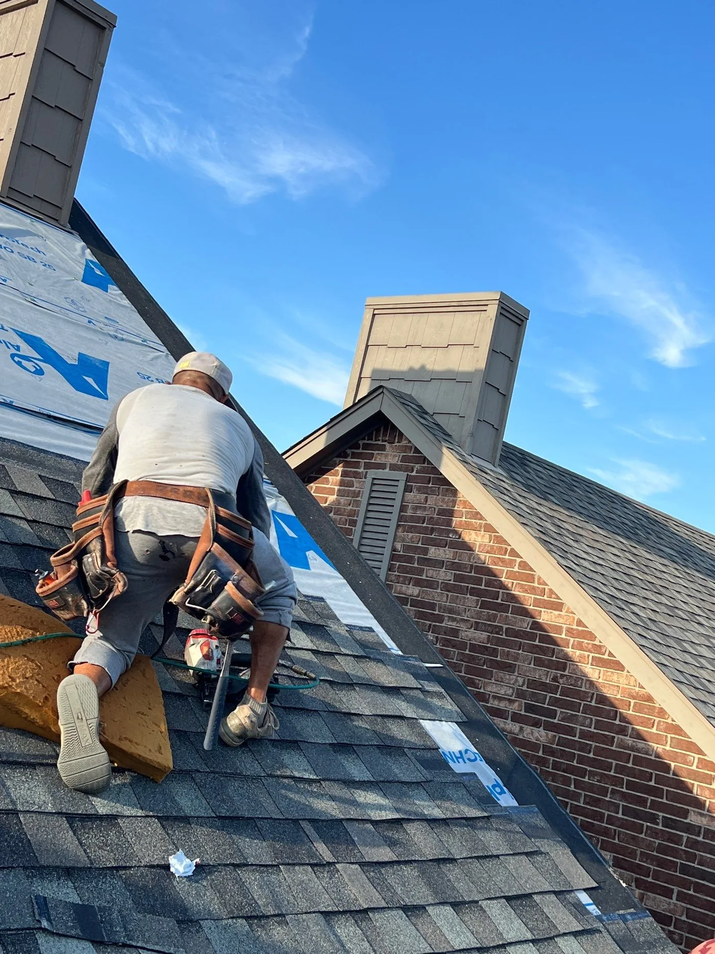FireHouse Roofing installer nailing architectural shingles near a brick gable end on a Tulsa home