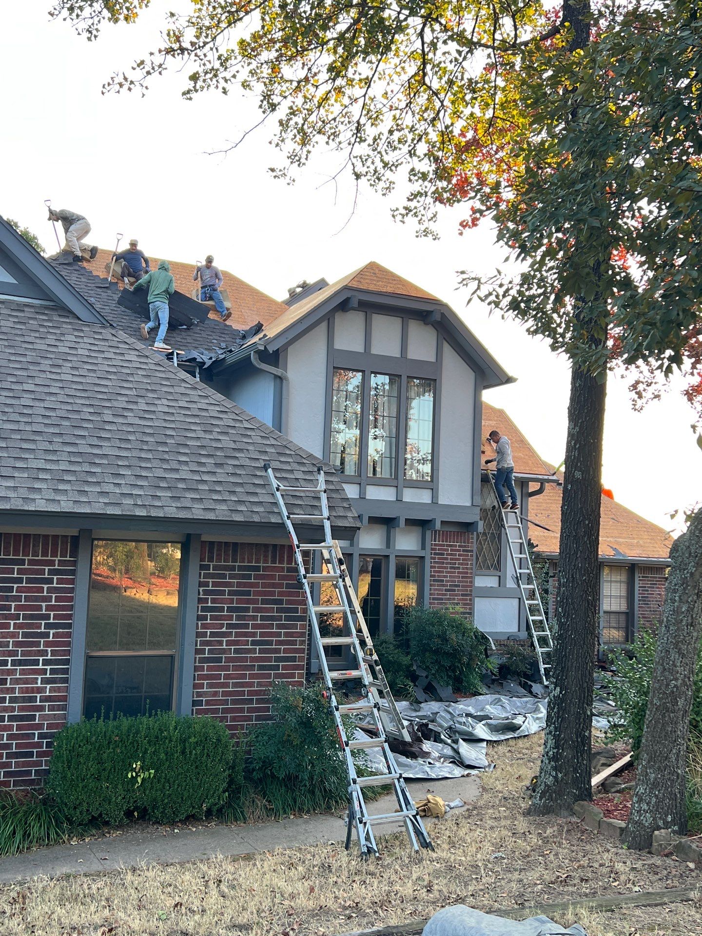 FireHouse Roofing crew mid-tear-off on a Sapulpa brick Tudor home, removing old shingles down to decking