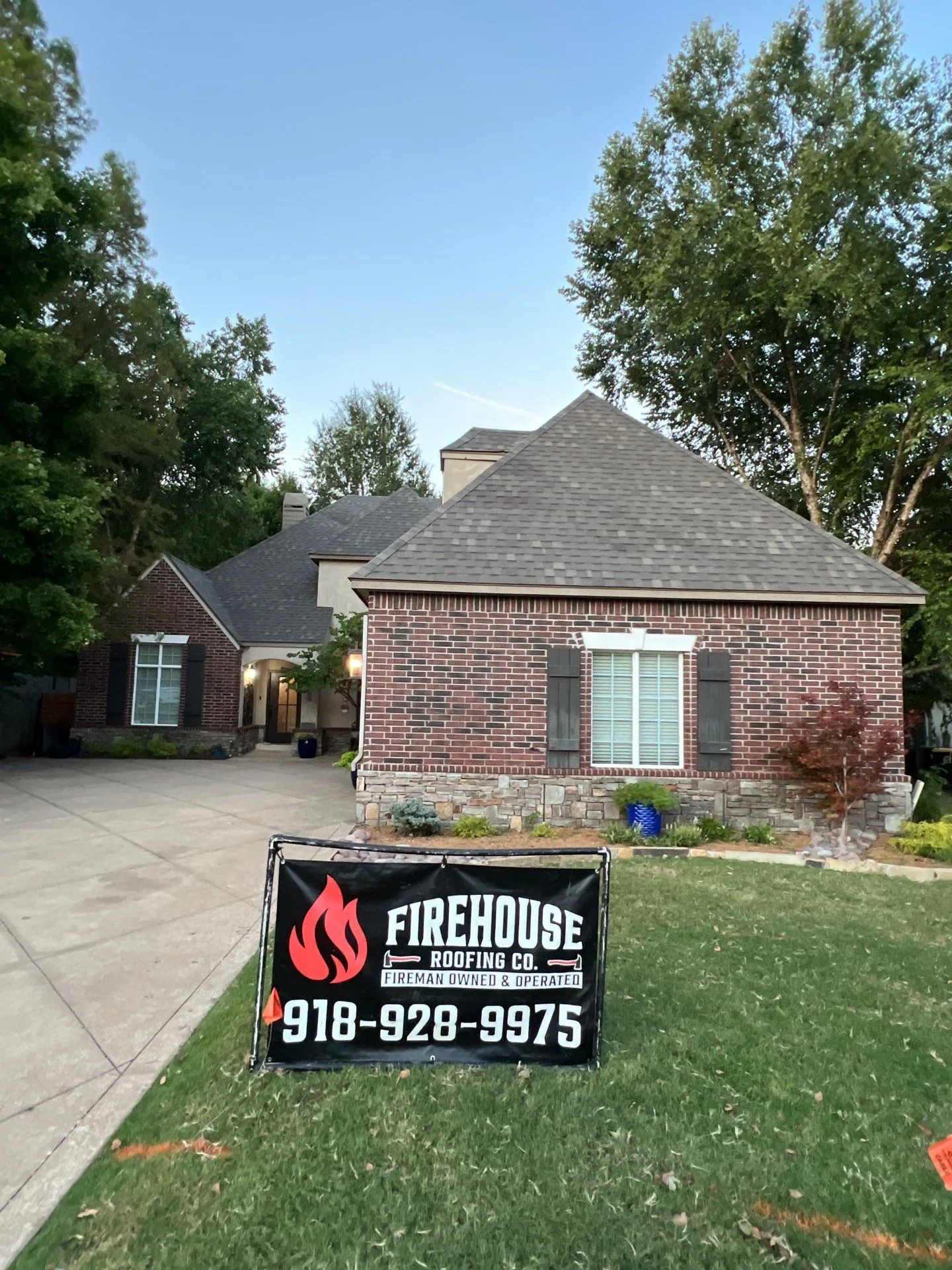 Red brick Tulsa home with a finished architectural shingle roof and a FireHouse Roofing yard banner out front