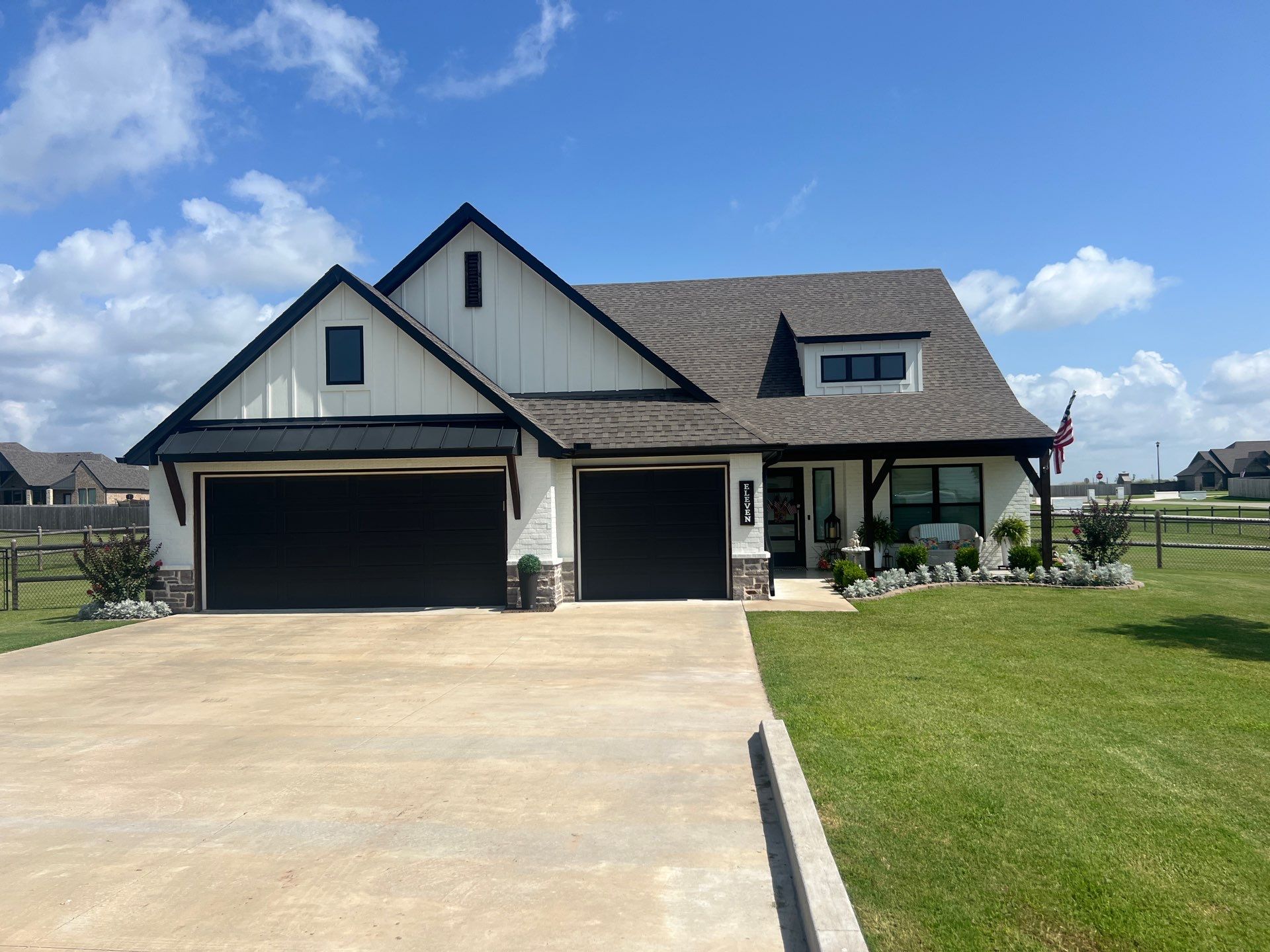 Completed roof replacement on a Glenpool white board-and-batten craftsman home with black accents and an American flag