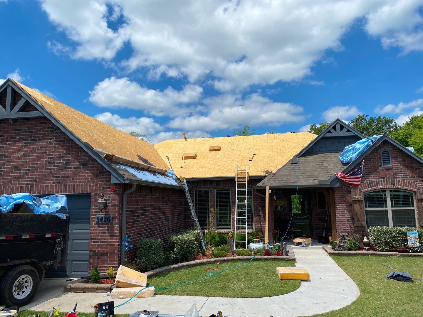 FireHouse Roofing crew mid-replacement on a Sand Springs brick home showing fresh decking and underlayment