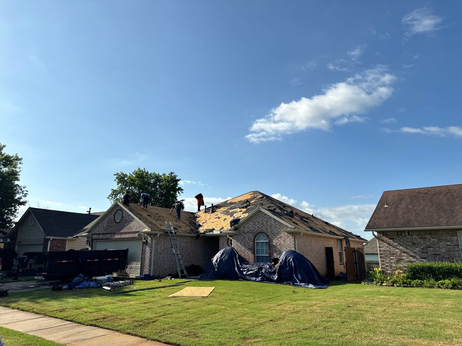 FireHouse Roofing crew mid-tear-off on a Glenpool brick ranch, removing old shingles down to decking with dump trailer staged in the driveway