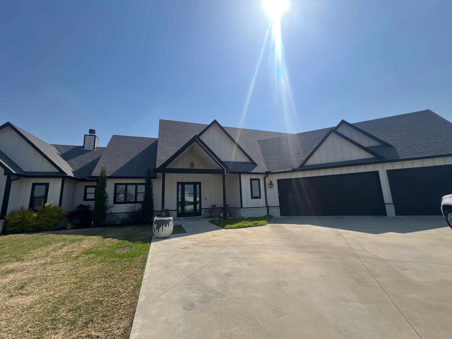 Completed roof replacement on a Glenpool white board-and-batten ranch with black trim and steep gables