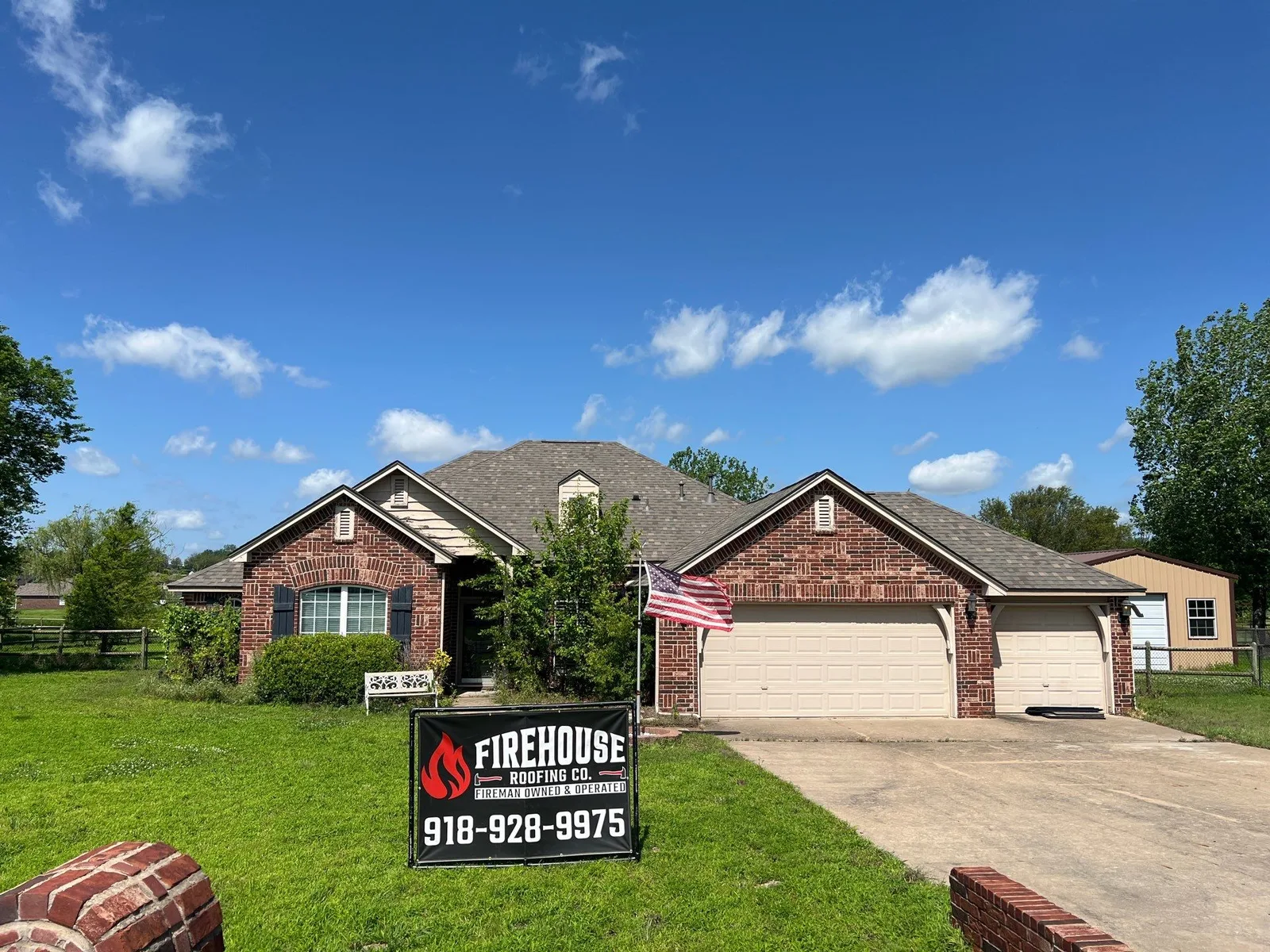 Collinsville brick home with American flag and FireHouse Roofing yard banner after roof replacement
