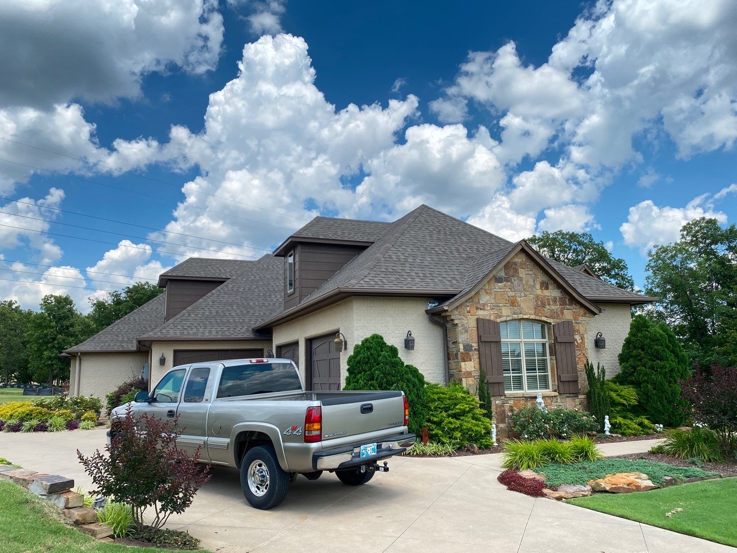 Completed FireHouse Roofing roof replacement on a Sand Springs stone and brick home with brown architectural shingles