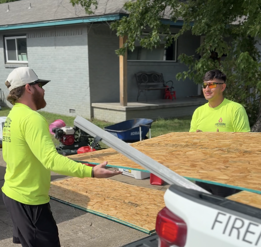 Two FireHouse Roofing crew members unloading OSB decking from a company truck