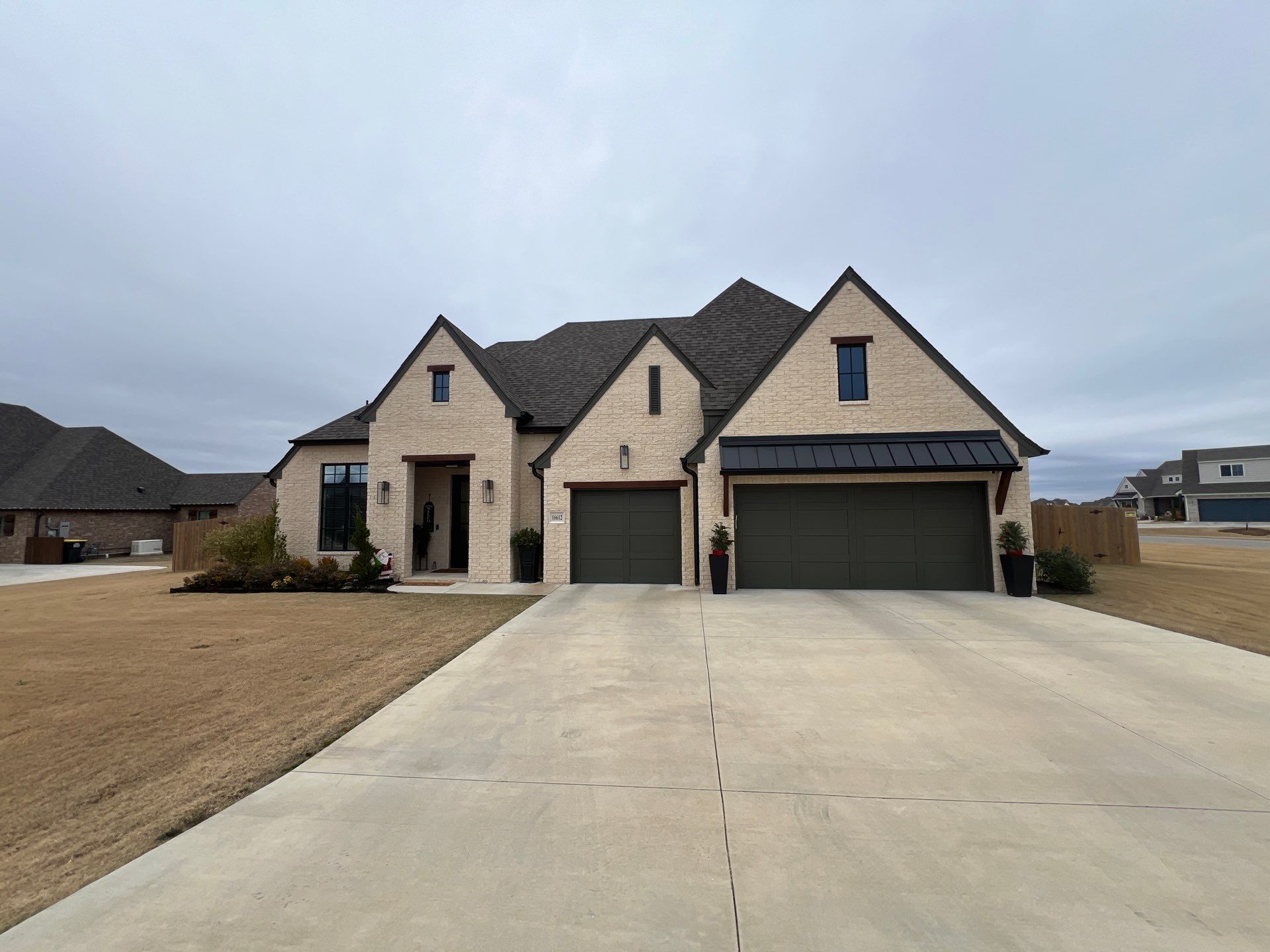 Completed roof replacement on a Glenpool stone Tudor-style home with dark architectural shingles and a 3-car garage