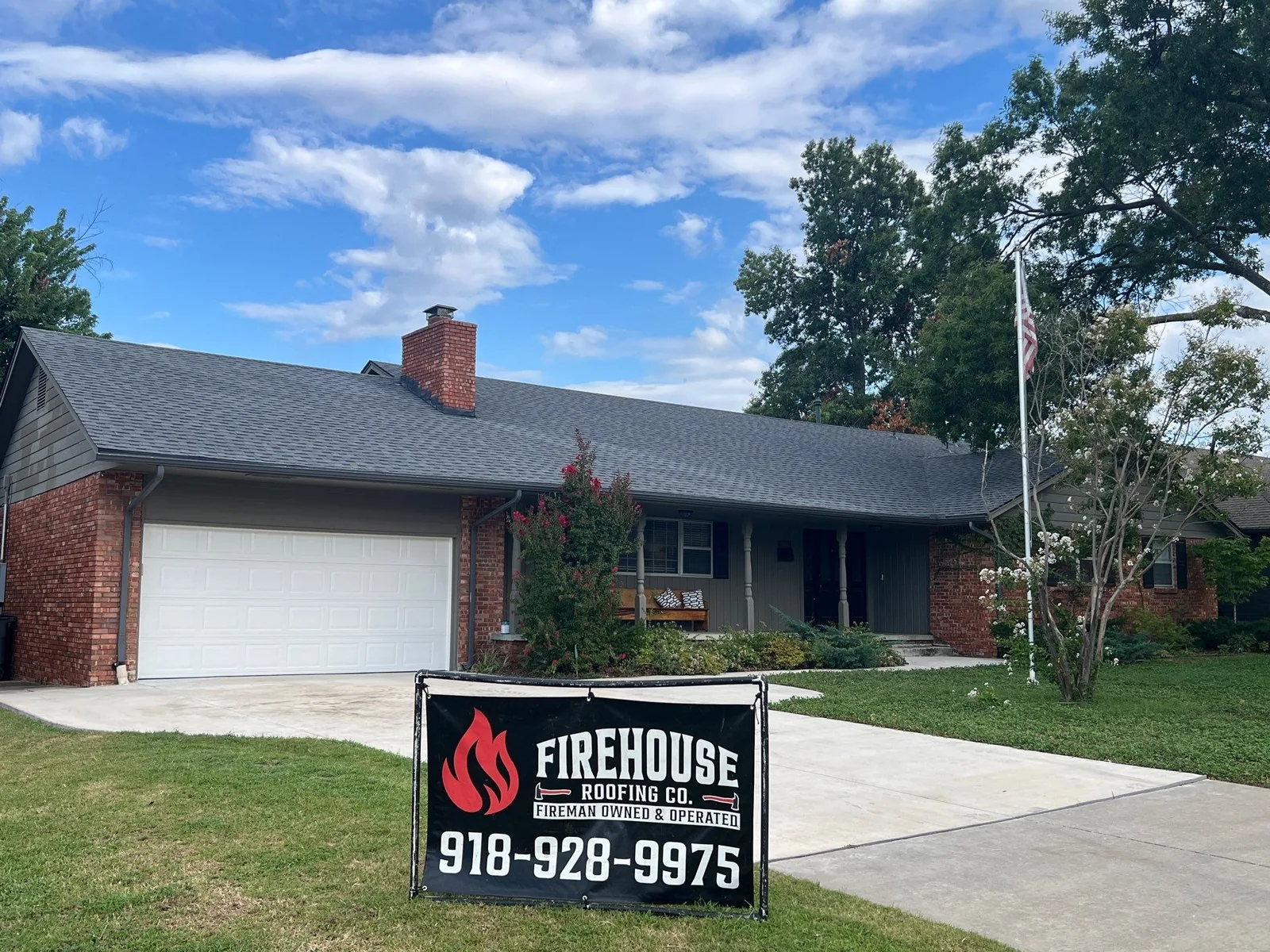 Finished gray architectural shingle roof on a brick ranch in Tulsa with a FireHouse Roofing yard banner